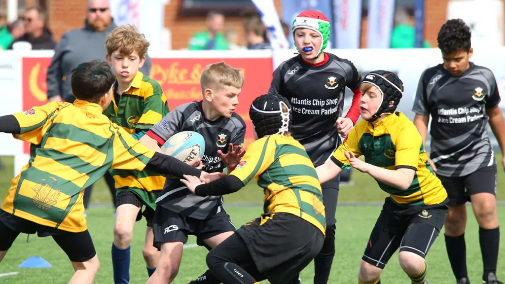 A player with the ball runs into opposing players whilst his team watch from behind