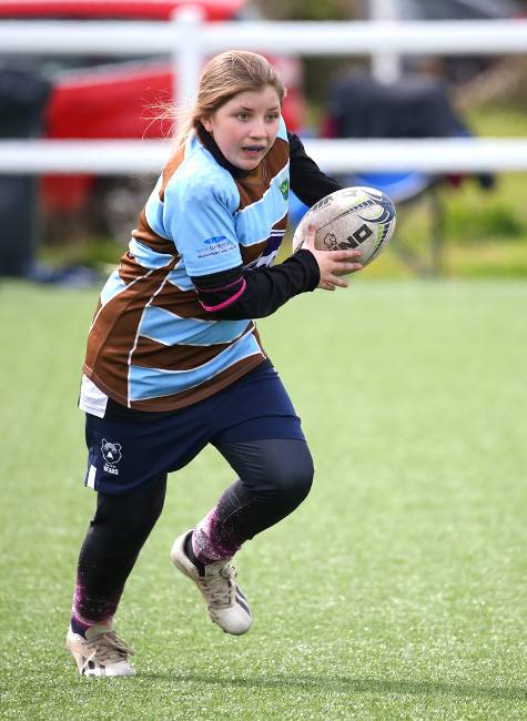 A girl rugby player runs with the ball