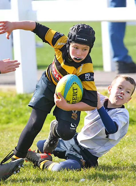 One rugby player pushes past another falling player in a competitive match