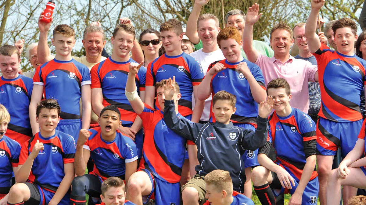 Boys rugby team and fans cheer and pose the camera.