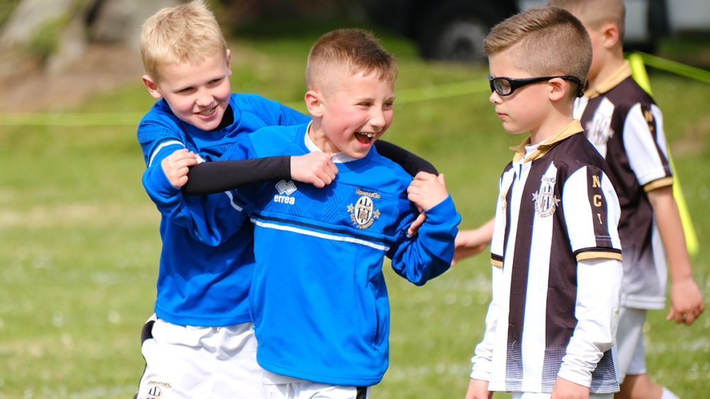 Two boy players celebrate whist an opposing player walks behind them