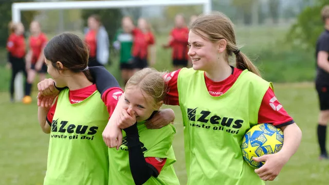 Three girl players in training bibs joke around