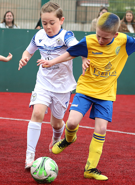 Two players compete for the football on a red astro turf pitch