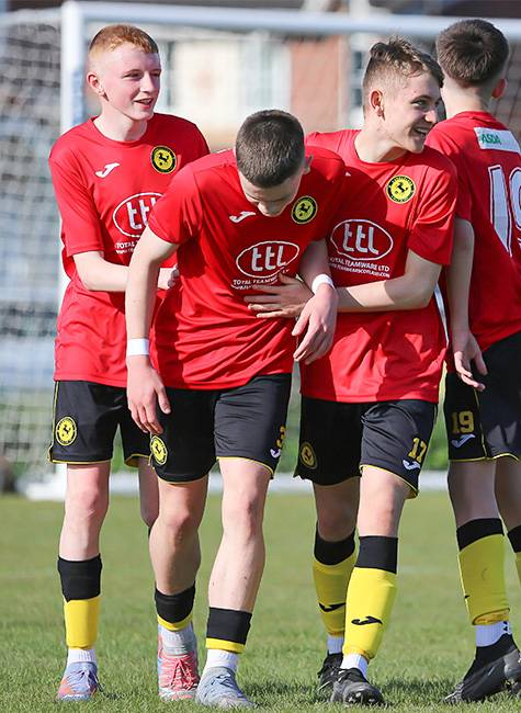 Players congratulate their team-mate with a football goal in the background.