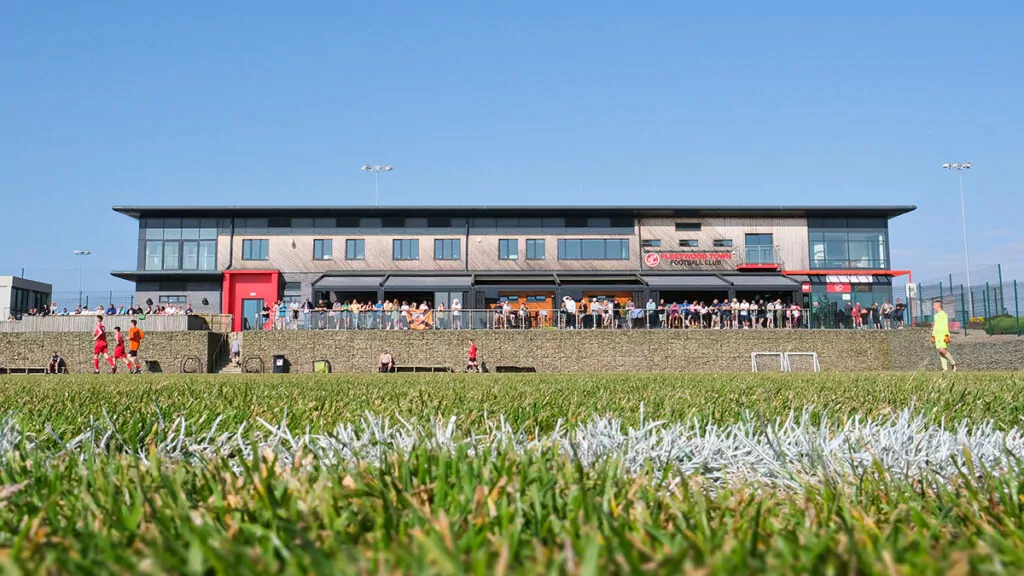 Green football pitch with main Poolfoot Farm building in the background