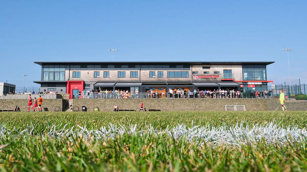 Green pitch with main Poolfoot Farm building in the background and whilst football match is played