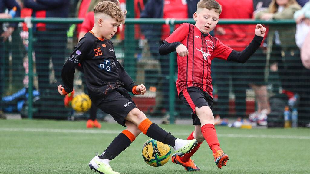 Two opposing kids go for the football as onlookers watch