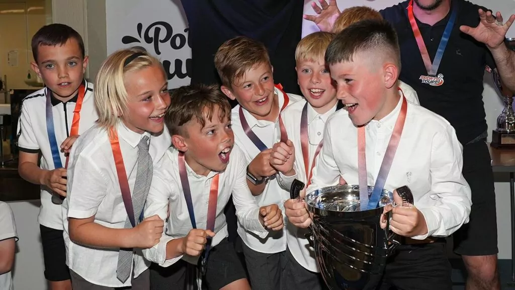 A football team, smartly dressed, celebrate around the Sports Tours trophy