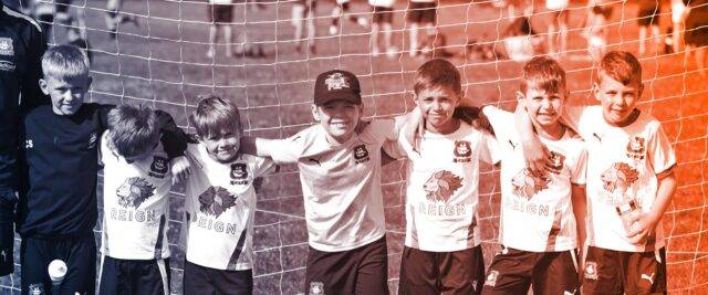 Kids football team pose in front of a goal net.