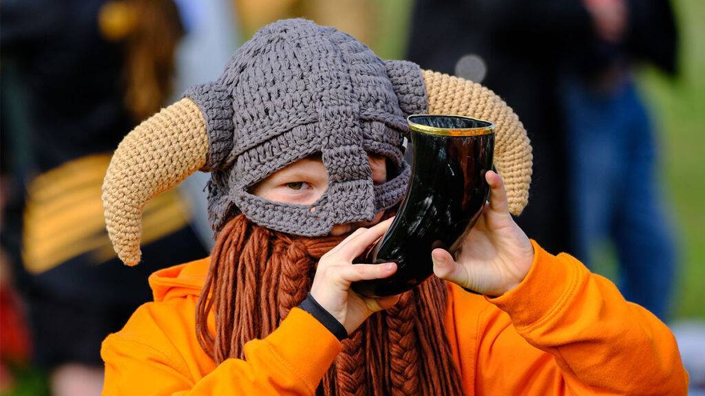A rugby fan wears a Viking helmet and blows a horn