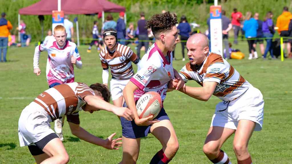 Two rugby players tackle an opposing player from the front and back