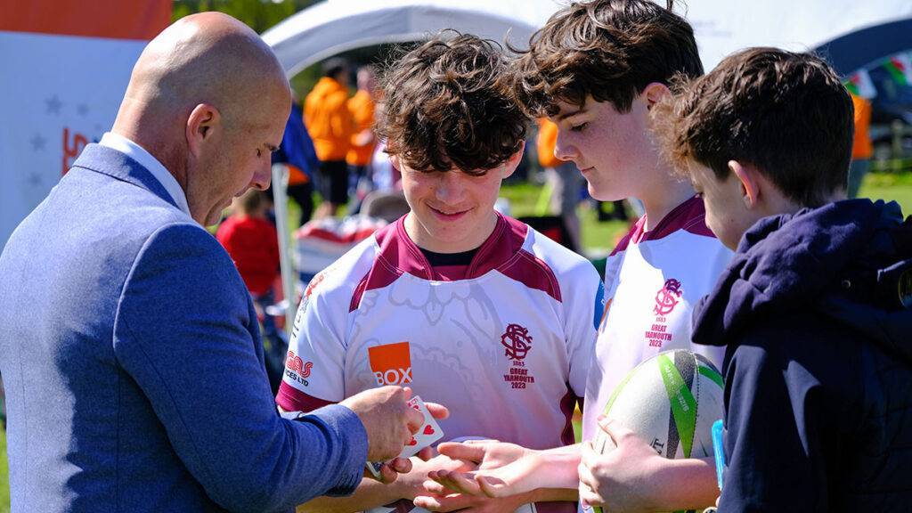 A magician performs a card trick to boy rugby players