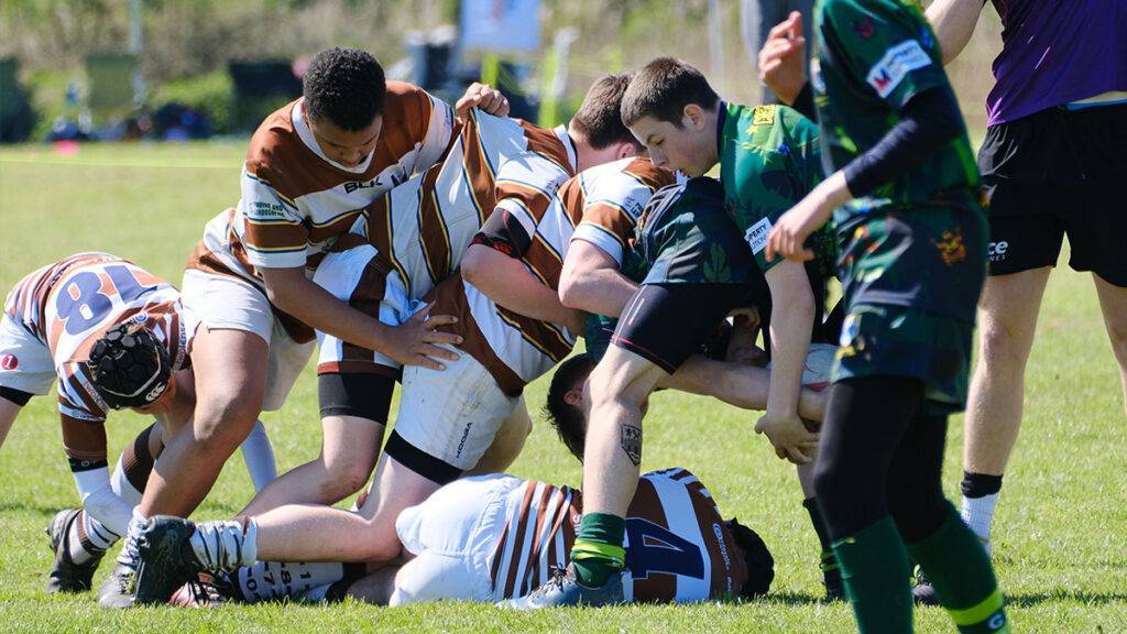 Two rugby teams compete for the ball, with one rugby player on the ground
