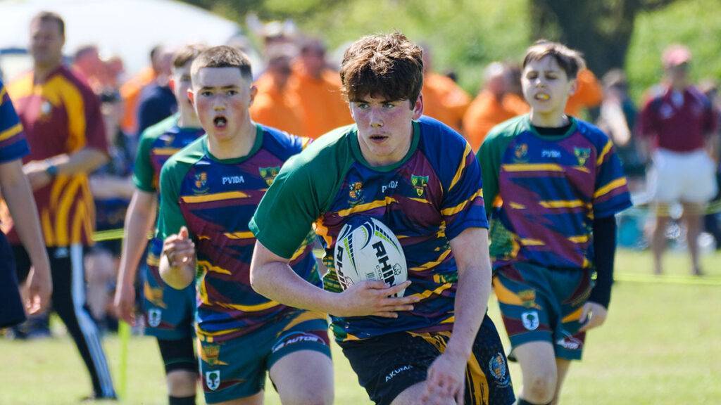 A rugby players runs with the ball as his team watches on