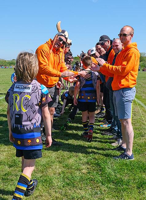 A guard of honour from adults, in orange hoodies, for a children's rugby team