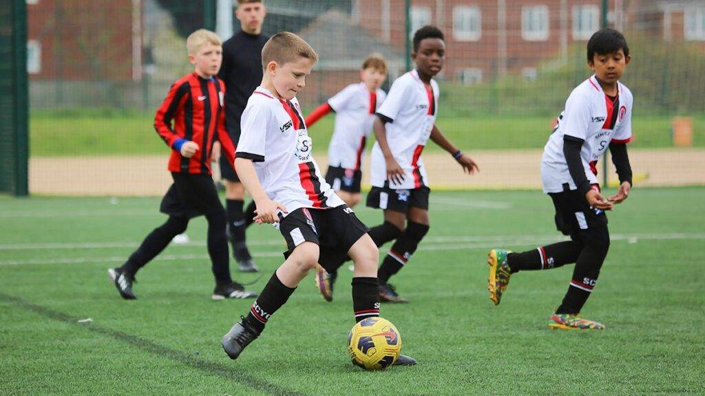 A player passes the ball, with his team and an opposing player in the background