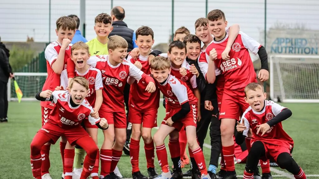 Children's football team celebrate with football pitches and goals in the background