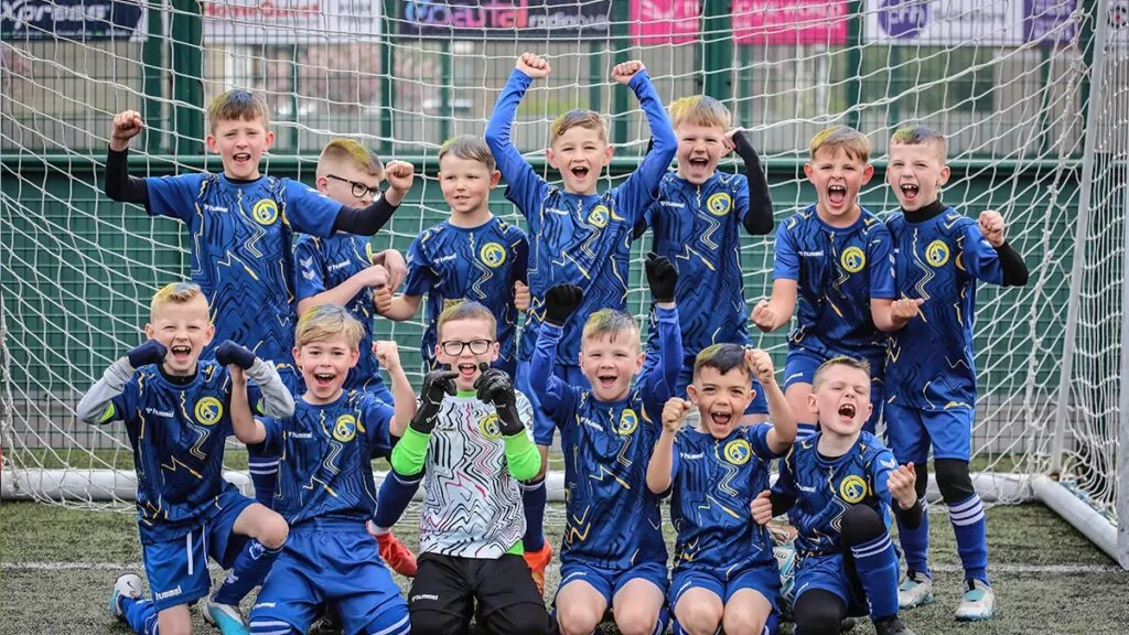 Kids team pose and celebrate in front of a football goal