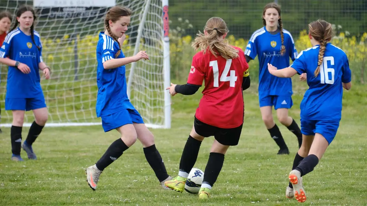 A footballer from a grassroots team dribbles the ball through the opposition players.