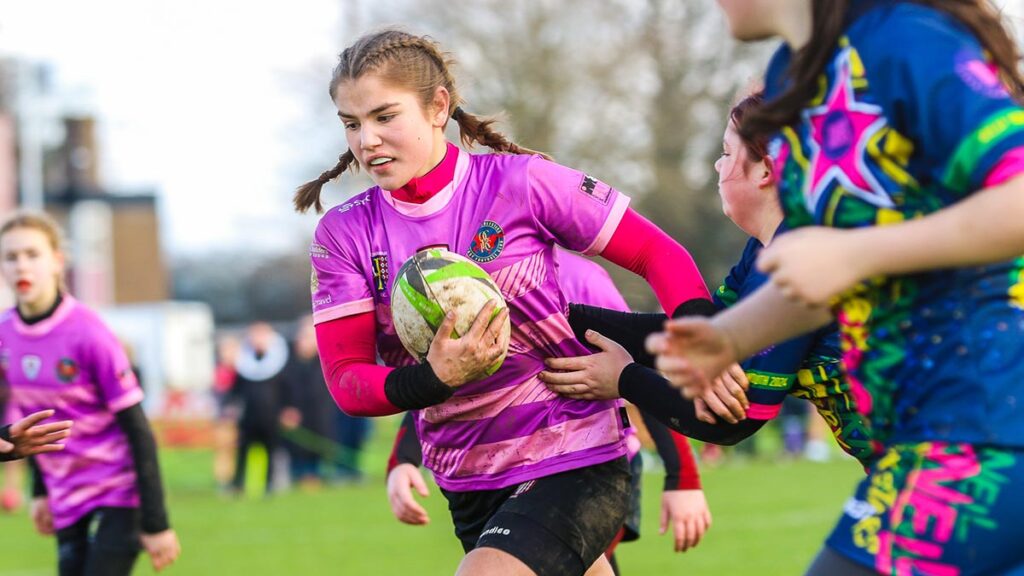A young girl rugby player running up field