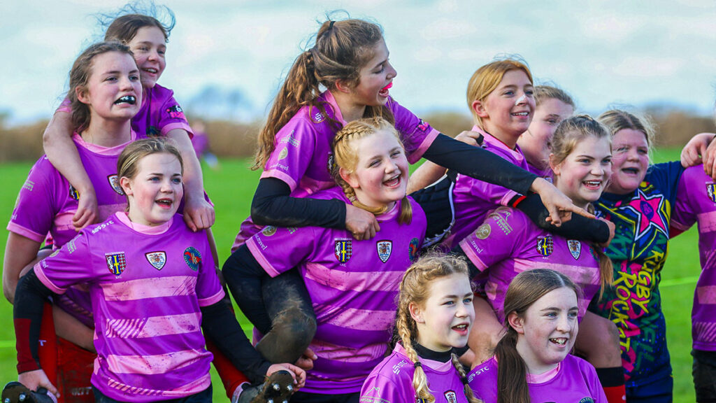 A young team of girls rugby players celebrating after a match