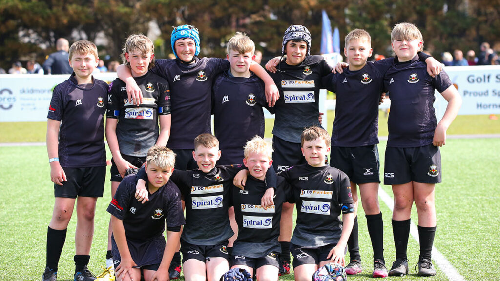 A team of youth rugby players pose for a group photo on a sunny day