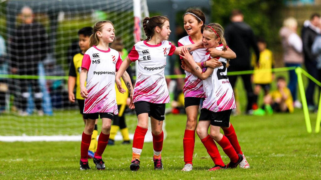 A young girls football team celebrating after a goal