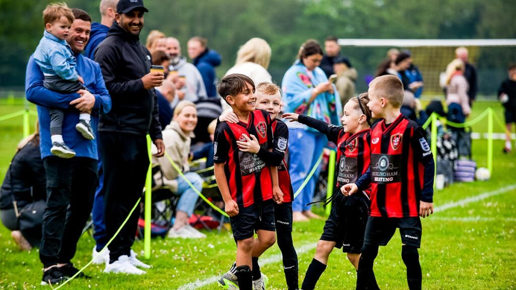 A young football team celebrating on the side line with some family members smiling