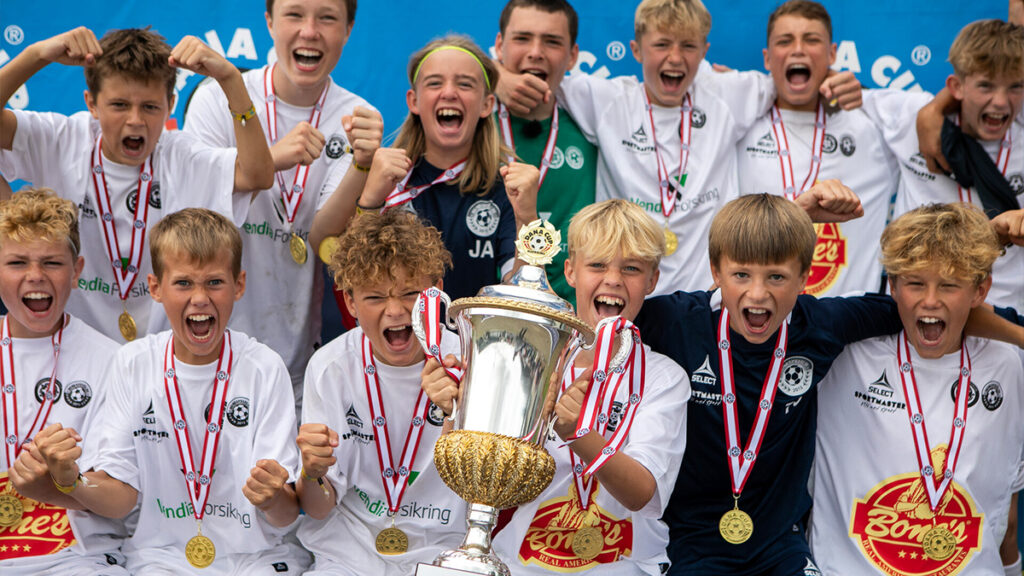 A young football team celebrate their win with a trophy on stage at the Dana Cup football tournament