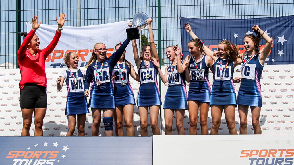 A team of young netball players celebrating on stage with a trophy