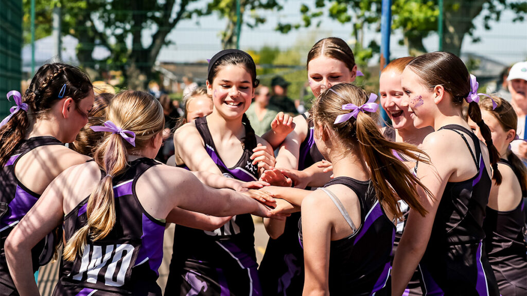 A young netball team put their hands in after tactics talk before a match