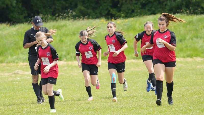 A group of young female footballers jogging to warm up before a game