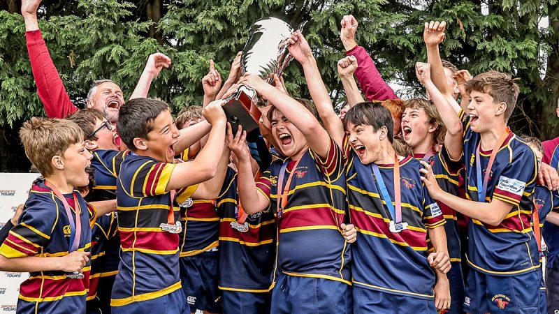 A young rugby team celebrate after a festival with their trophy
