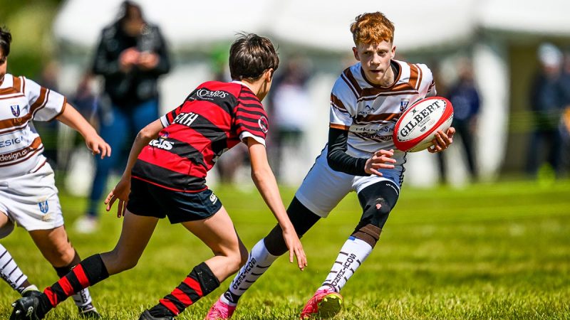 A young rugby player steps to the side of another to get the ball further afield